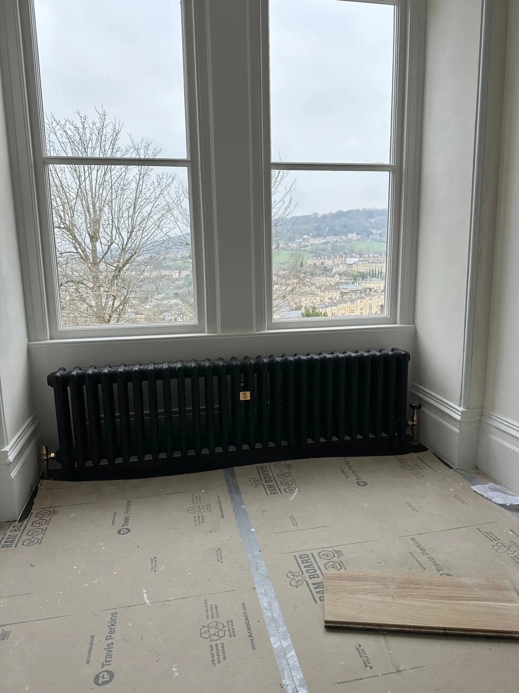 Cast iron column radiator fitted beneath a bay window in a period property, with brass valves and the floor protected